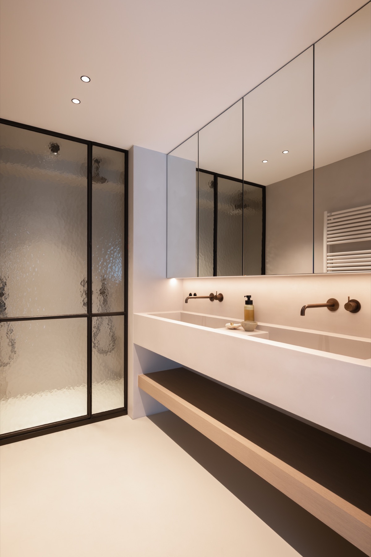 Badkamer met brede lavabo, bronzen kranen en douche met gegolfd glas